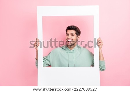 Portrait of positive funky young man arms hold paper album set card look empty space isolated on pink color background