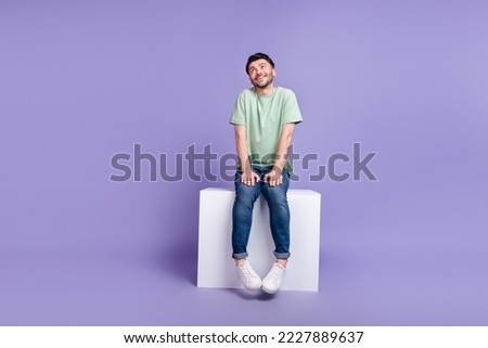 Full size photo of handsome young guy sit shy pose white cube look empty space wear trendy gray outfit isolated on violet color background Royalty-Free Stock Photo #2227889637