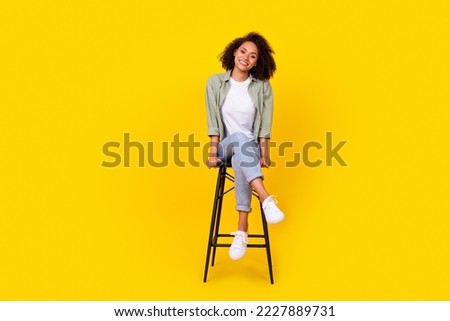 Full size photo of cheery young woman curly hair sit chair have rest chatting wear trendy khaki outfit isolated on yellow color background