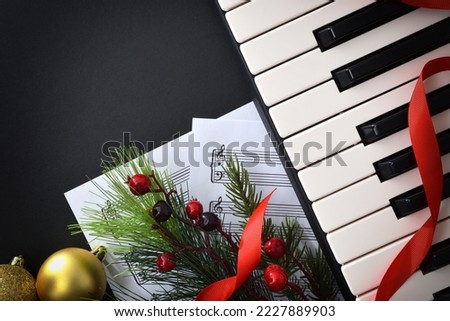 Conceptual detail of Christmas performance of piano with instrument and sheet music and Christmas decoration on black table. Top view.