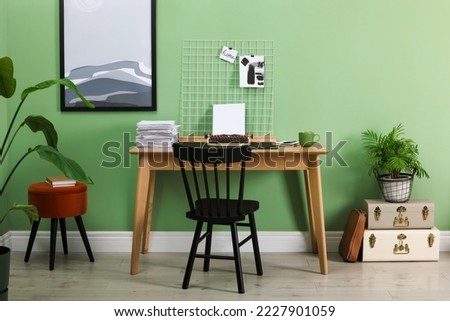 Typewriter, stack of papers and mood board on wooden table near pale green wall. Writer's workplace