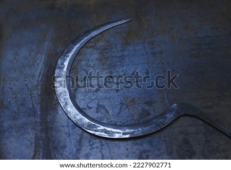 A thin metal sharpened sickle lies on a background of a sheet of bluish metal.