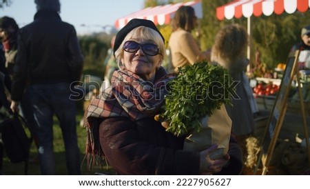 Senior woman in sunglasses stand with bag of vegetables, posing and looks at camera, spending leisure time outdoor. Weekend on farmers market.