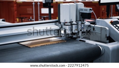 Digital laser die cut machine cutting corrugated cardboard. Industrial manufacture. Royalty-Free Stock Photo #2227912475