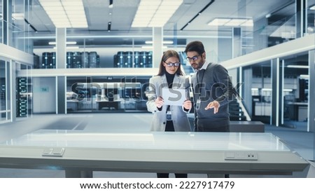 Factory Office Meeting Room: Chief Engineer Holds Tablet Computer, Showing Augmented Reality 3D Software to Male Project Manager. They Test a Futuristic Project. Modern Industry 4.0 Research. Royalty-Free Stock Photo #2227917479