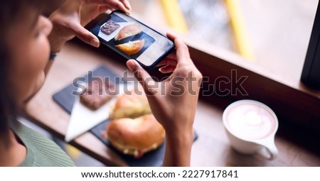 Woman In Coffee Shop Taking Picture Of Food To Post On Social Media