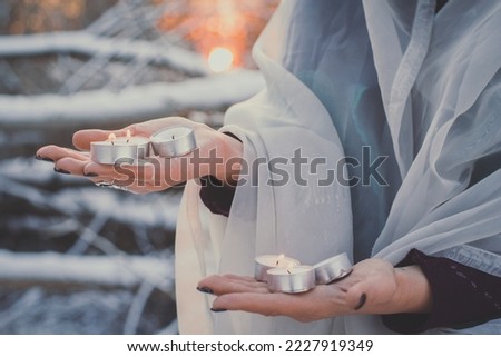 Close up hands with candles concept photo. Melting wax on palms. Side view photography with winter forest on background. High quality picture for wallpaper, travel blog, magazine, article