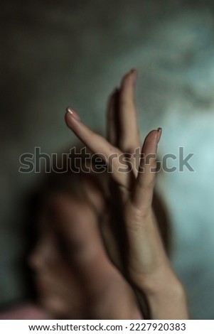 Close-up of beautiful female hand with simple nail manicure on gray background, selective focus. Long fingers and a fragile wrist, plastic movement on the background of a face and a gray wall.
