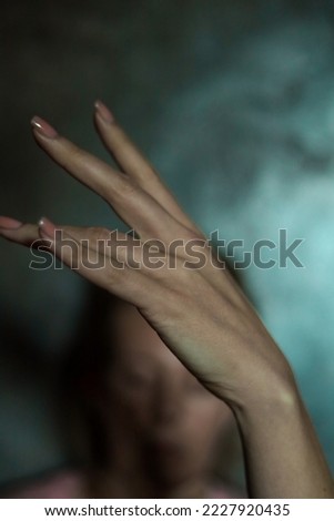 Close-up of beautiful female hand with simple nail manicure on gray background, selective focus. Long fingers and a fragile wrist, plastic movement on the background of a face and a gray wall.