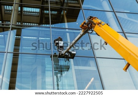 Cleaner worker using a cherry picker to clean a glas facade of a contemporary office building. Royalty-Free Stock Photo #2227922505