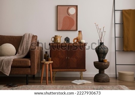 Interior design of cozy living room interior with mock up poster frame, brown sofa, stylish sideboard, vase with dried flowers, round pillow, books, plaid, pumpkin and personal accessories. Home decor