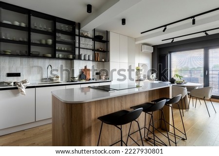 Modern composition of kitchen interior with kitchen island, stylish black chockers, built-in kitchen, glass cabinets, grey table and personal accessories. Home decor. Template. 
