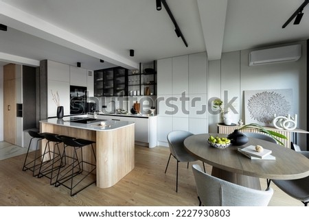 Modern composition of kitchen space with design kitchen island, black hookers, grey table, flowers, furnitures, big window and elegant personal accessories. Stylish home decor. Template