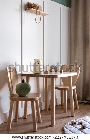 Warm and cozy kids room interior space with wooden table, chairs, green stuffed toy, white wall, white bear, simple gray curtain and personal accessories. Home decor. Template. 