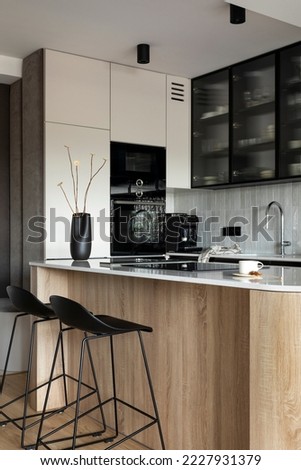 Modern composition of kitchen space with design kitchen island, black hookers, grey table, black vase with dried flowers, furnitures, and elegant personal accessories. Stylish home decor. Template.
