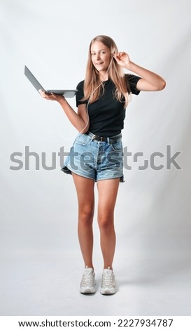 Beautiful smiling young woman standing over a grey background using a laptop computer with earphones