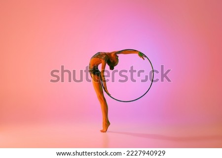 Young flexible teen girl rhythmic gymnast in motion, action isolated over pink background in neon light. Sport, beauty, competition, flexibility, active lifestyle. Individual performance
