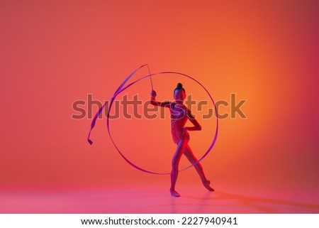 Young flexible teen girl rhythmic gymnast in motion, action isolated over pink background in neon light. Sport, beauty, competition, flexibility, active lifestyle. Individual performance