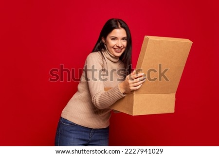 Surprise, happy women's day. Young beautiful girl holding gift box isolated on red background. Concept of positive emotions, holidays, inspiration, sales, ad.