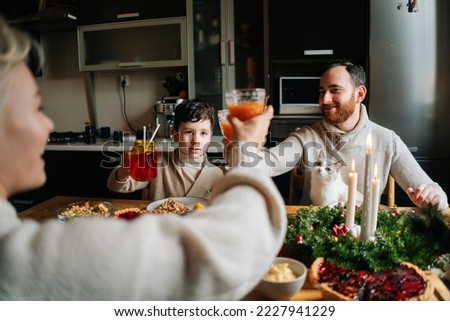 Close-up view from back to cheerful Caucasian family with adorable little child boy clinking glasses toasting at festive table during holiday family party, selective focus, blurred background.