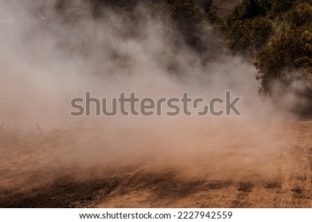 A dust storm. Powdered dust and sand flowing into air on a gravel road. Concept of extreme weather events, rally and offroad races. Copy space.