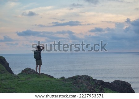 Silhouette of a man standing on a hill and taking a picture on landscape background in Bukit Merese, Lombok, West Nusa Tenggara, Indonesia.