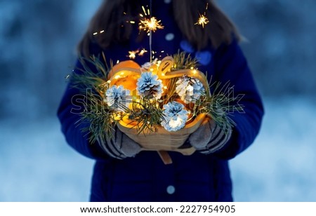 Christmas wooden basket on the street in the hands with tangerines, cones with lights on a background of snow. Festive picture selective focus. Bengal fire new year mood