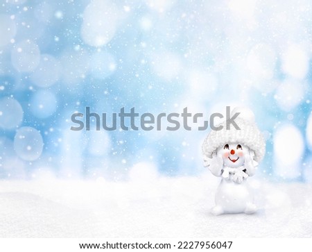a snowman in a hat stands on the snow on a blue background with bokeh