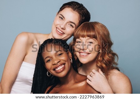 Portrait of women with different skin tones smiling at the camera in a studio. Group of happy young women feeling comfortable in their own skin. Three body positive young women standing together. Royalty-Free Stock Photo #2227963869