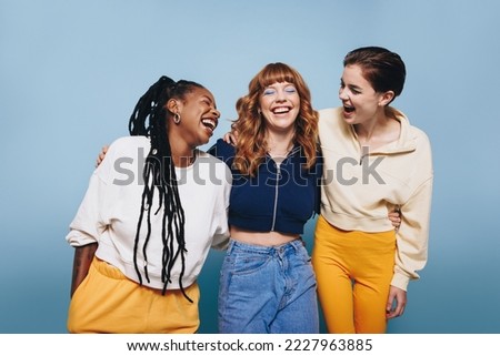 Happy young women laughing together in a studio. Group of female friends having fun while standing together. Royalty-Free Stock Photo #2227963885
