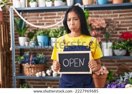 Hispanic woman working at florist holding open sign depressed and worry for distress, crying angry and afraid. sad expression. 