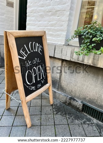 sign board in front of a shop or cafe door. chalk board with open sign at street, entrance of a shop says welcome, we are open come on in on black board