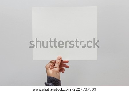 Woman's hand holding a white blank paper, mock-up over the white wall