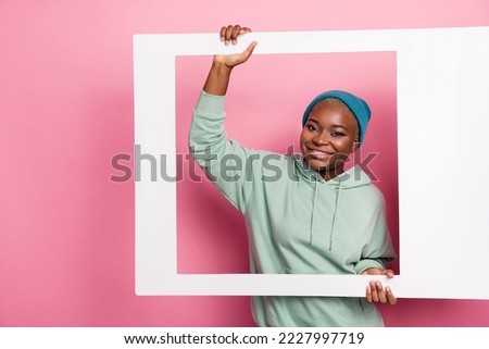 Portrait of young adorable girl holding big white polaroid frame picture of herself isolated on pink color background