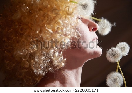 Portrait of woman in white blonde wig with dandelions. Female model posing in studio for dark picture with light