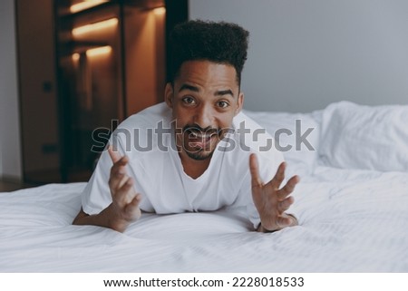 Young surpised amazed smiling happy cool man of African American ethnicity in nightwear lying in bed relax spend time in bedroom lounge home in own room house wake up dream be lost in reverie good day Royalty-Free Stock Photo #2228018533
