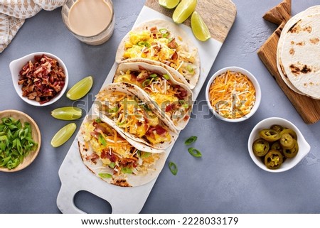 Breakfast tacos with hashbrowns, scrambled eggs and bacon topped with cheese and green onion, overhead shot