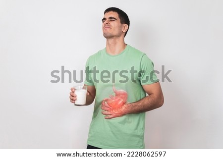 Lactose intolerance. A young man holds a glass of milk in his hand and suffers from severe abdominal pain.Problem with dairy products, White studio background. Royalty-Free Stock Photo #2228062597