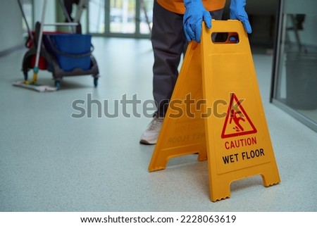 Mindful janitor putting plastic caution sign on the wet floor