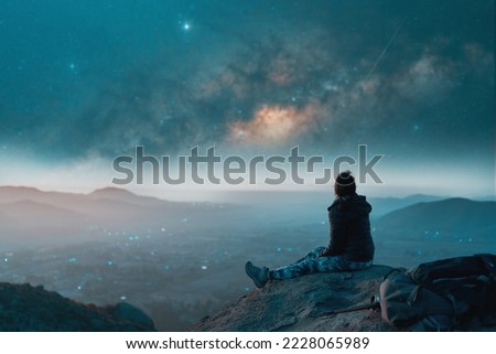 silhouette of a young woman sitting on top of the hill watching a shooting star in the dark sky over the valley