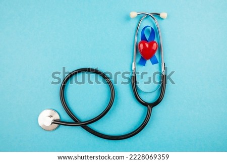 Top view photo of stethoscope and blue ribbon with small red heart, prostate cancer awareness symbol on isolated pastel blue background with copy space