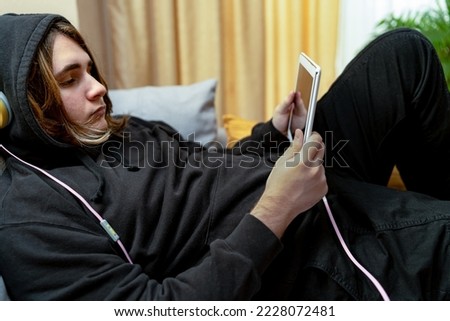 Teenager who spends time lying on the sofa or in his bedroom consuming internet and social networks. Concept of internet and social media addiction. Royalty-Free Stock Photo #2228072481