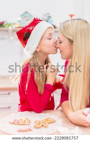 Cute little girl enjoys christmas time and kisses her mom on the nose in the kitchen while preparing christmas cookies