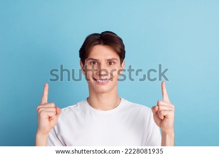 Handsome young man pointing away up looking at camera with smile while standing against blue background.