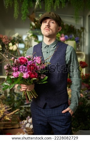 Attractive cheerful caucasian male in peaked cap and vintage clothes from 20s holding beautiful bouquet of red and violet flowers. Mother's Day or Valentine's Day concept. High quality image