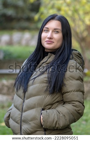 Street portrait of a happy beautiful woman of 30 years old with long black hair on a blurry neutral background of autumn nature.