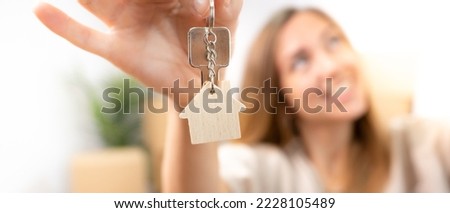 Happy young woman smiling with the new home keys keychain with wooden house real state banner. High quality photo