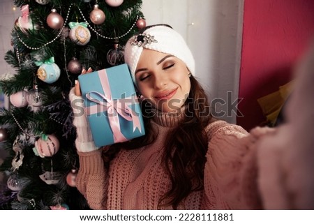 A happy young woman with a gift in her hand takes selfies against the Christmas tree. Merry Christmas and happy holidays New Year and Christmas concept.
