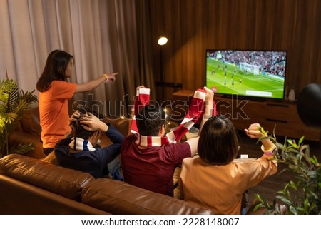 Group of Asian people friends sit on sofa watching and cheering football or soccer games competition on TV together at home.Happy man and woman sport fans celebrating sport team victory sports match Royalty-Free Stock Photo #2228148007