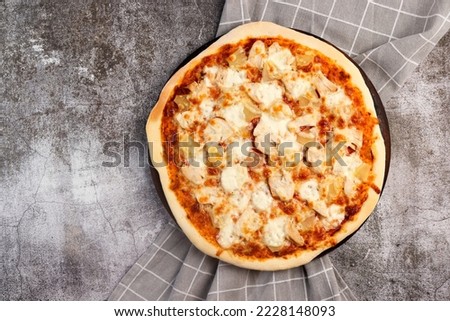 Homemade pizza with chicken and pineapple on a round wooden cutting board on a dark grey background. Top view, flat lay